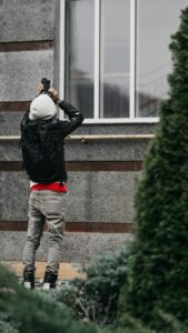 A homeowner checks roof shingles and gutters from the ground beside a snow-free house.